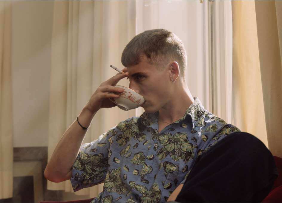 Slika prikazuje moškega, ki sedi pije kavo in ima prižgan cigaret v roki, odvajanje od kajenja je lahko zelo težko še posebaj, ko postane kajenje rutina