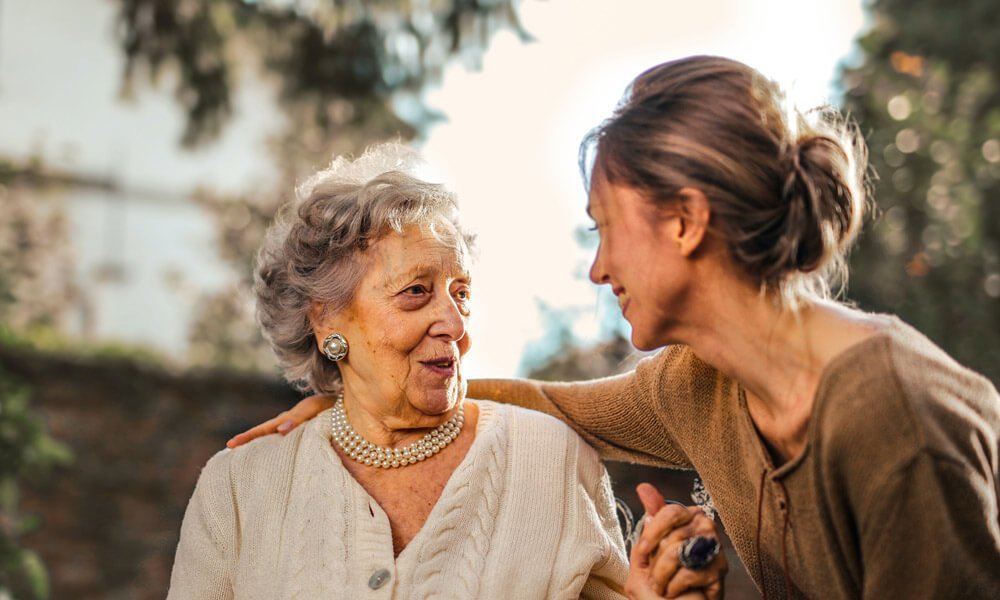 Slika prikazuje dve ženski, ki se pogovarjata in sta vidno nasmejane.