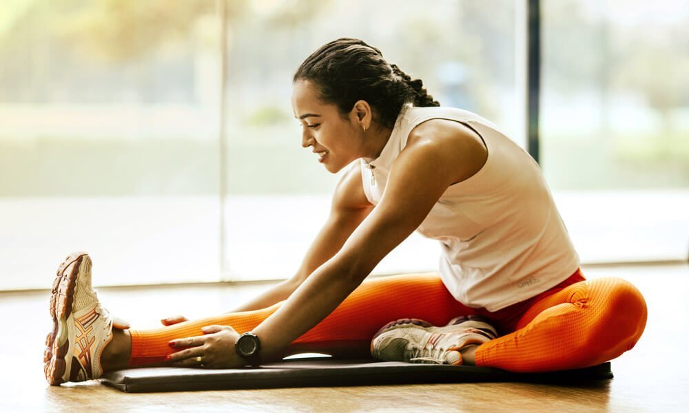 Na sliki je prikazana ženska, ki se razteguje pred ali po vadbi za uporabo članka CBG mazilo.